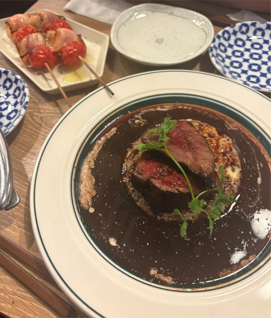 デミグラスソースのかかったステーキと、トマトの串焼きなどのおつまみ