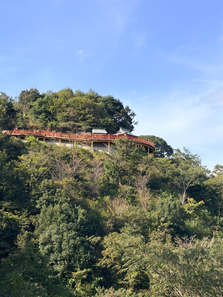 緑の木々に覆われた丘の上に、朱色の欄干がのぞく霞神社の遠景