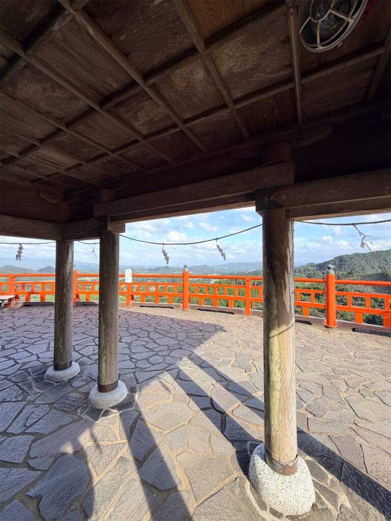 屋根のついた休憩所の柱の向こうに広がる、朱色の欄干と山の景色
