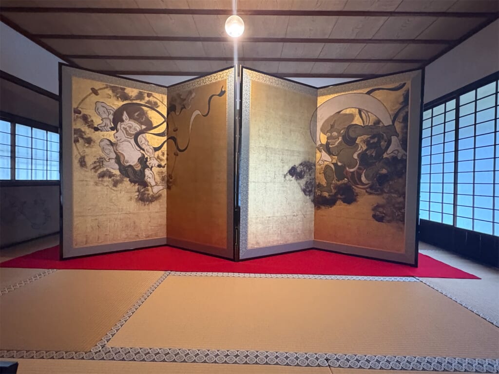 畳の間に置かれた金地の風神雷神図屏風の複製。左に雷神、右に風神