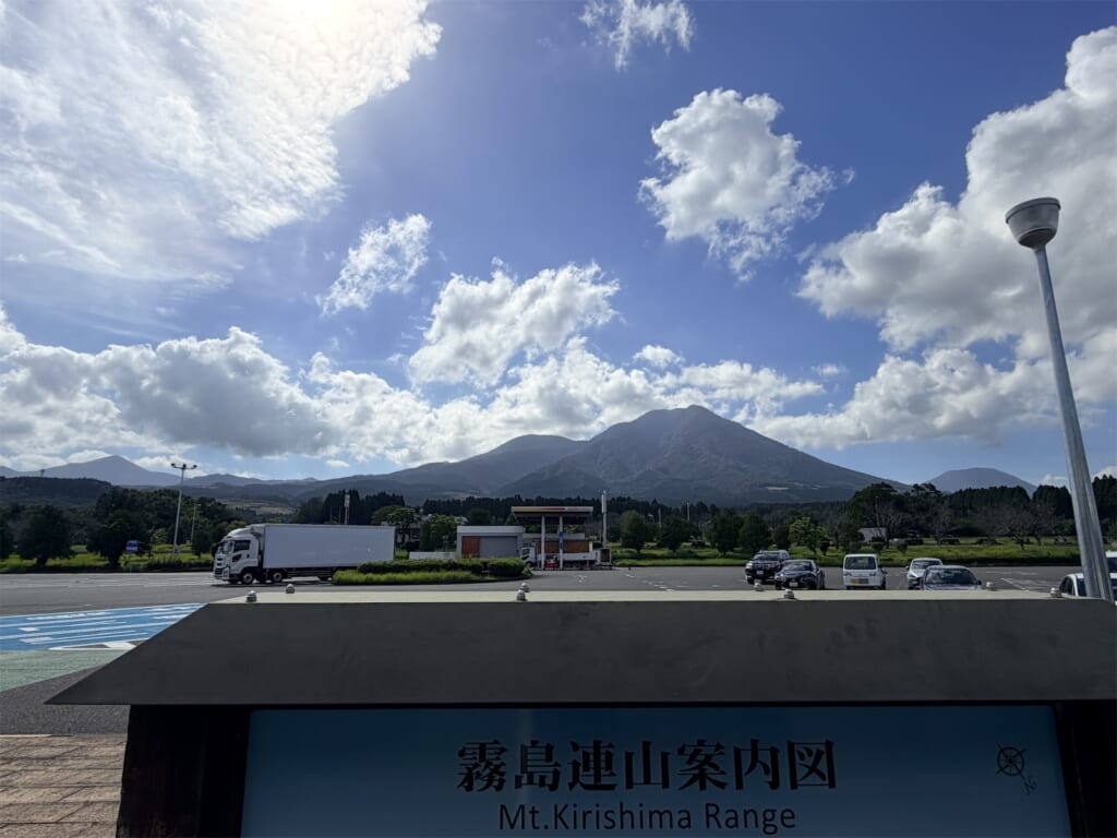 青空と白い雲の下に連なる霧島連山と、手前の霧島連山案内図の看板