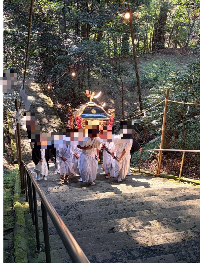 槵觸神社の石段を、白装束の担ぎ手が神輿を担いで上がってくる様子(参加者の顔はモザイク処理)