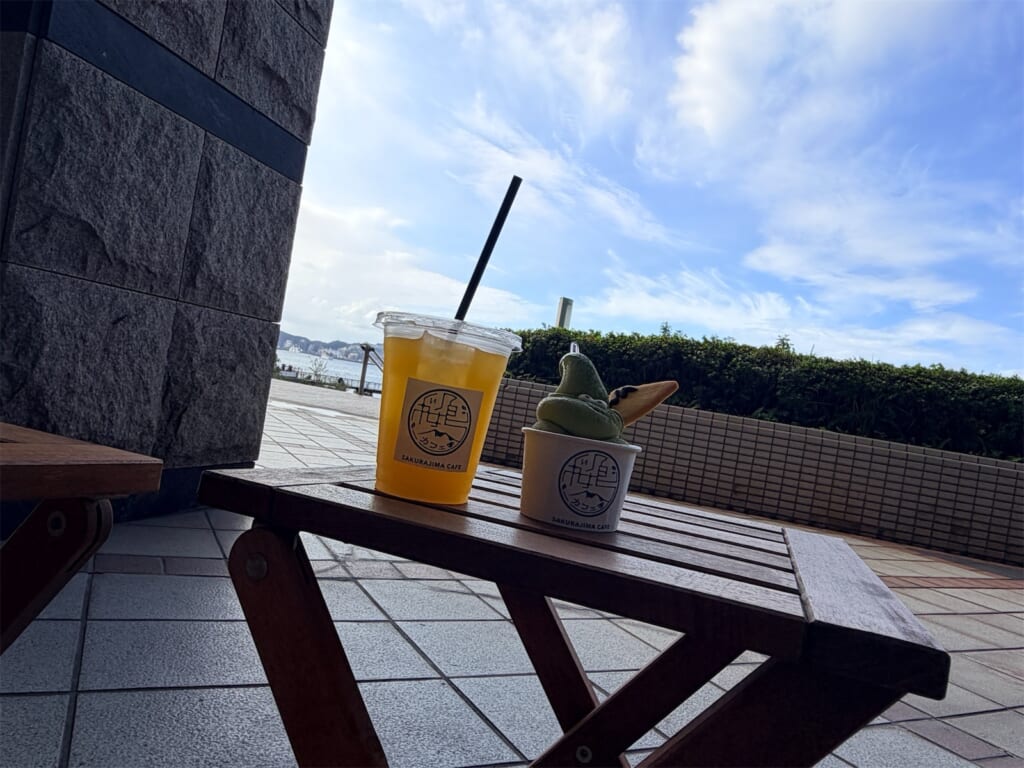 テラス席のテーブルに置いた、さくらじまかふぇの抹茶ソフトクリームと桜島小みかんジュース