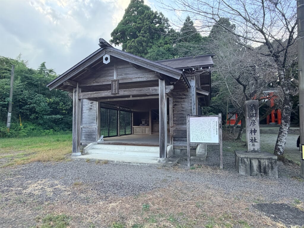 木造の猿田彦神社の社殿と、「猿田彦神社」と刻まれた石柱、案内板