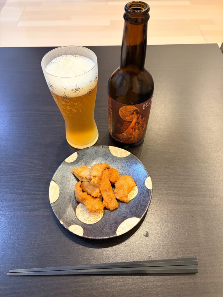 帰宅後、自宅のテーブルに置いたクラフトビールの瓶とグラス、皿に盛ったホルモン